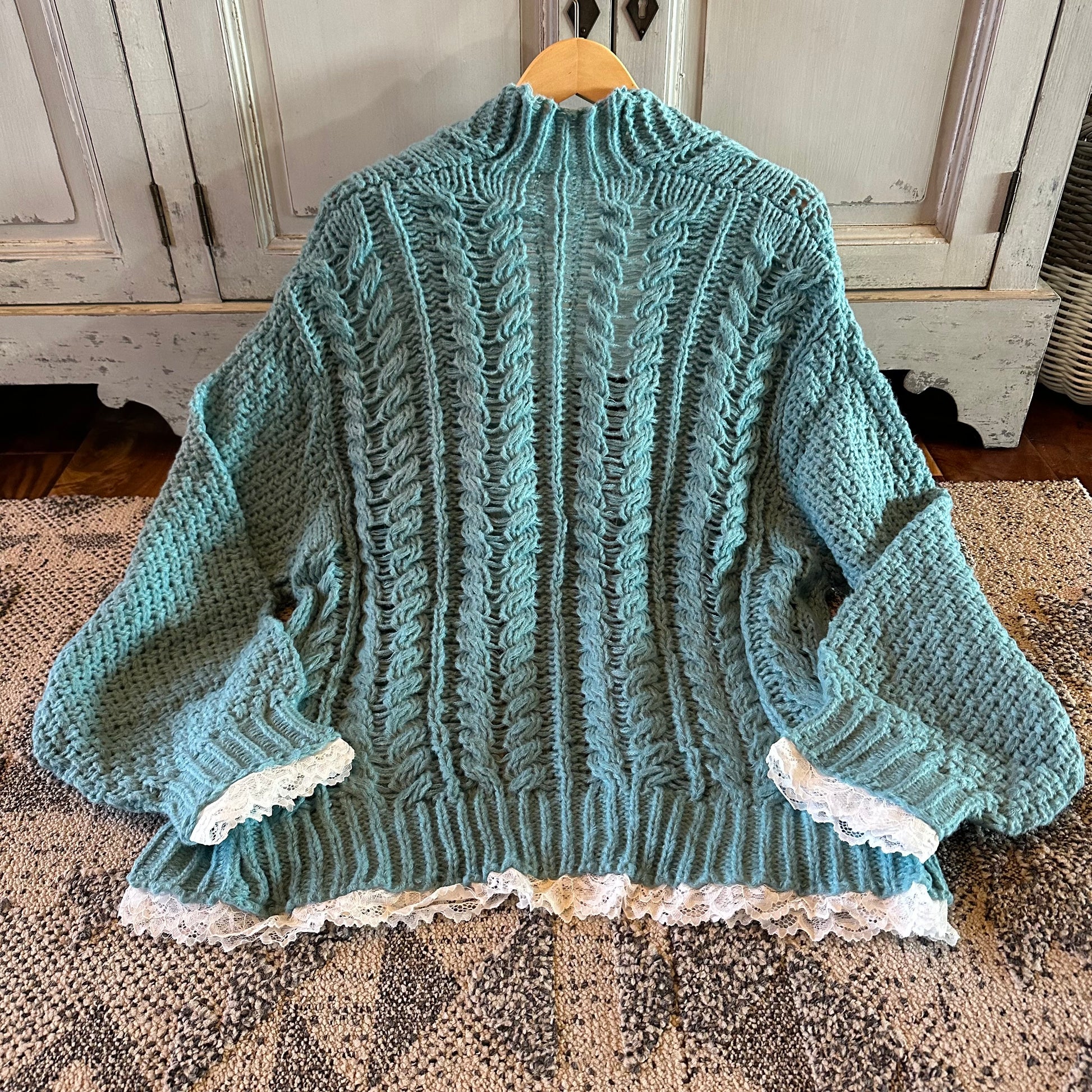 Teal knitted sweater with lace trim on a wooden surface