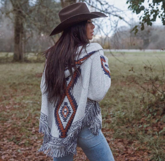 Woman wearing a patterned poncho and brown hat in an outdoor setting