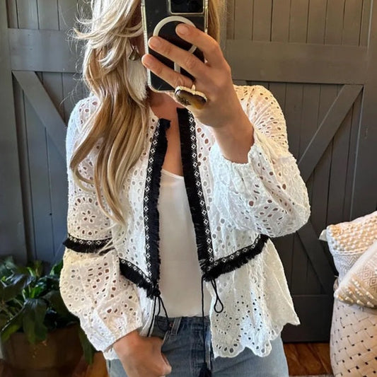 Woman wearing a white lace cardigan with black trim in a home setting.