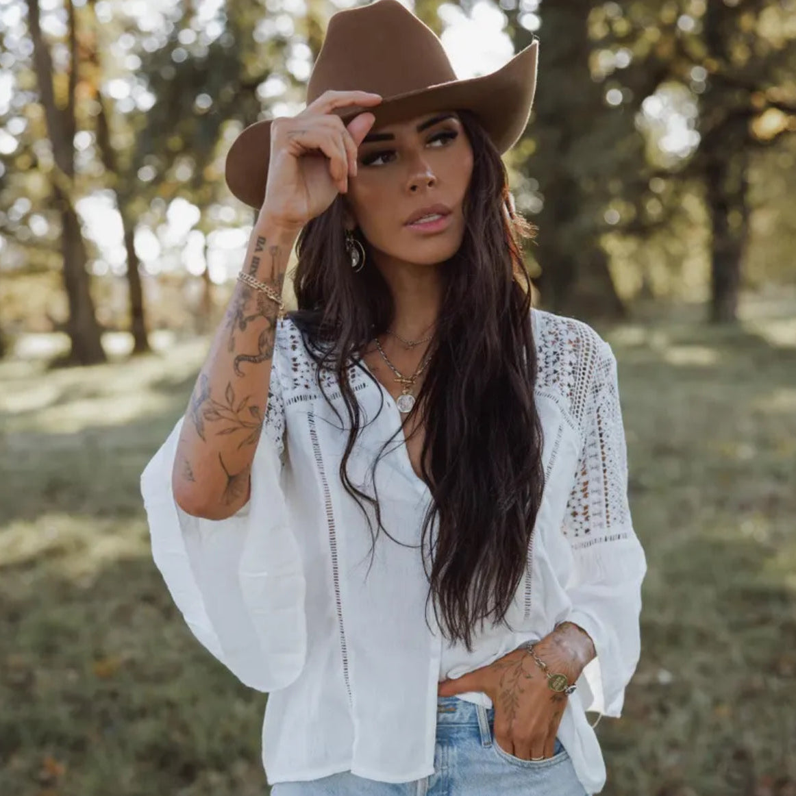 Woman wearing a brown cowboy hat and white blouse in a natural setting