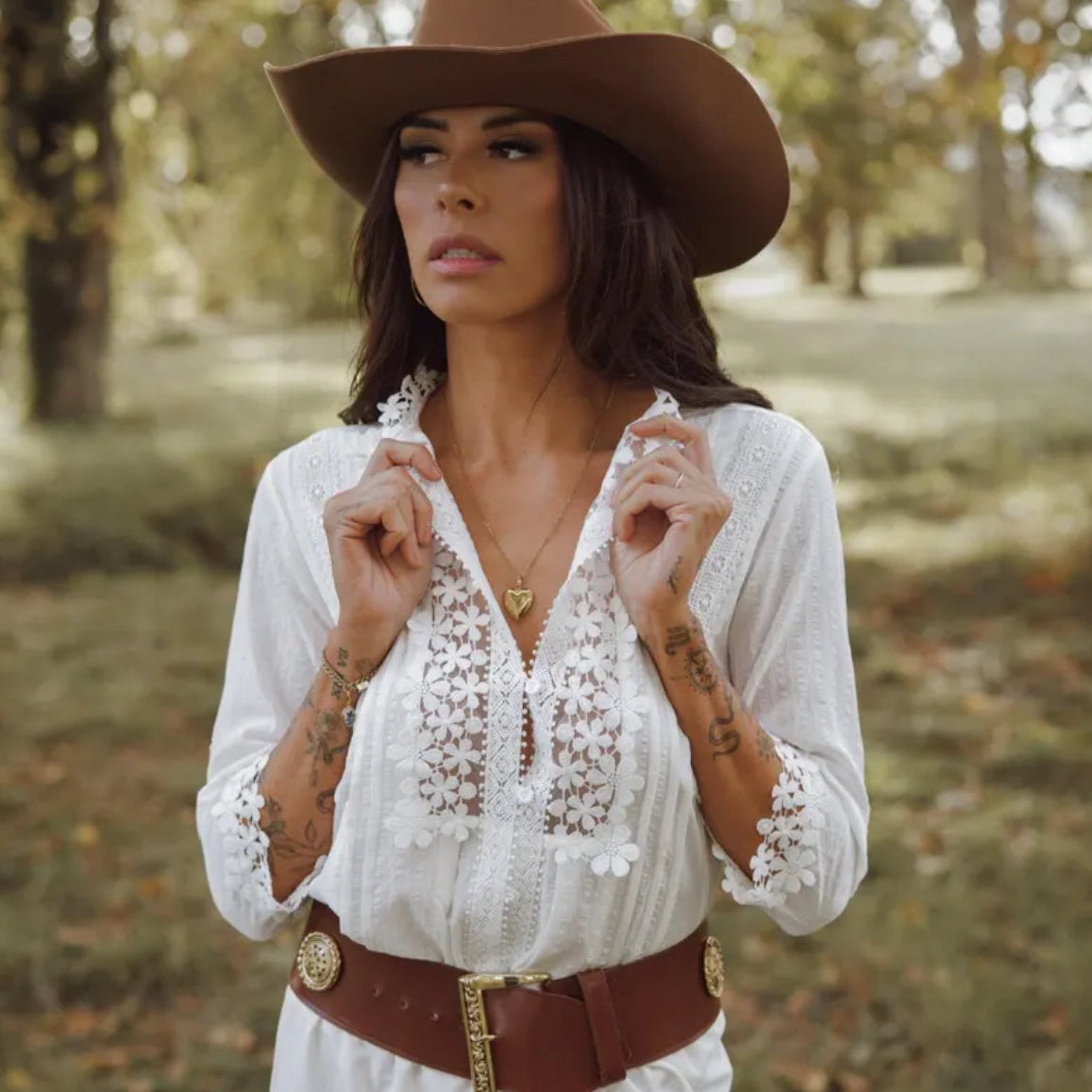 Woman wearing a white lace blouse and brown cowboy hat in a natural setting