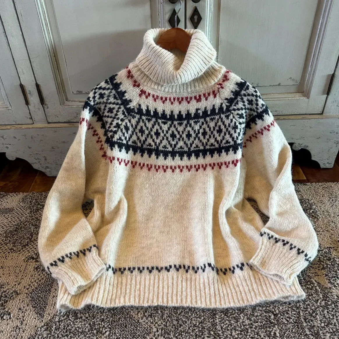 Beige sweater with a patterned design on a carpeted floor.