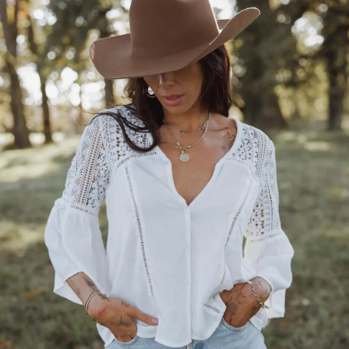 Woman wearing a white lace blouse and brown cowboy hat in a natural setting