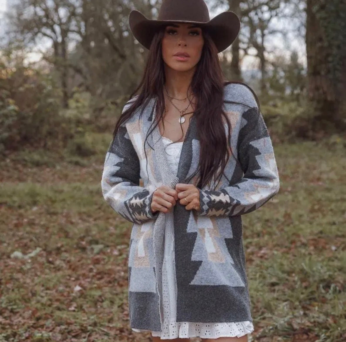Woman wearing a patterned cardigan and cowboy hat in a natural setting