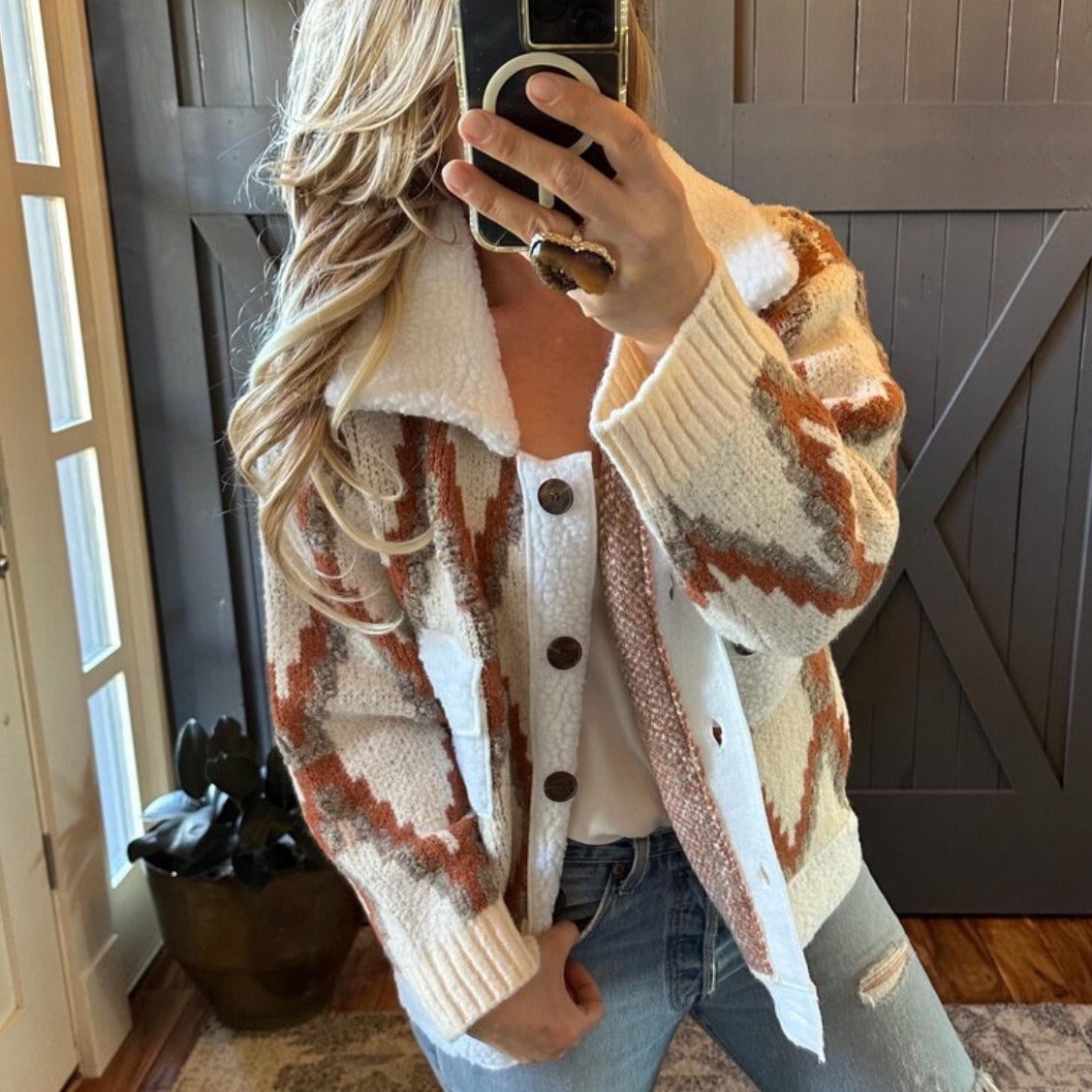 Person wearing a patterned cardigan taking a mirror selfie indoors.