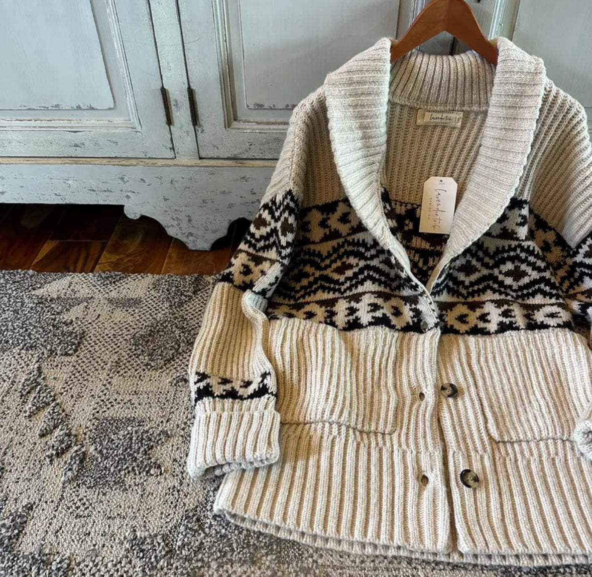 Knitted cardigan with patterned collar on a hanger against a wooden cabinet background