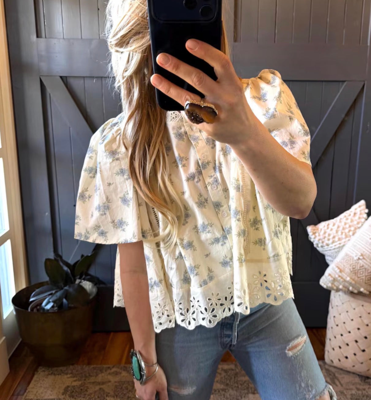 Person wearing a floral blouse and jeans taking a mirror selfie.