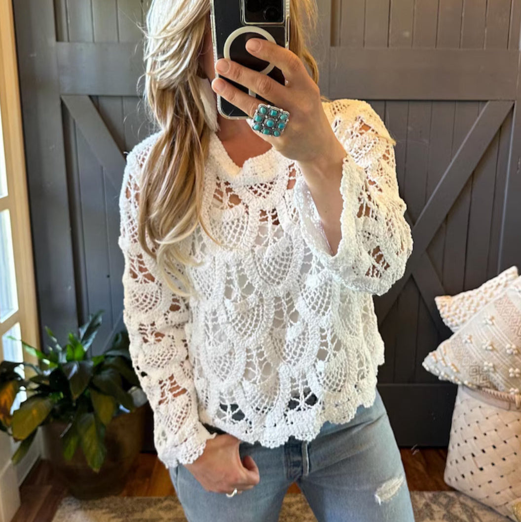 Person wearing a white lace top and jeans in a room with wooden walls and a plant.