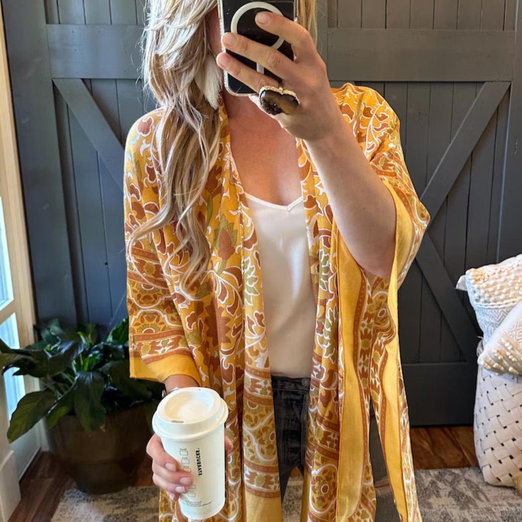Person wearing a yellow patterned kimono holding a coffee cup indoors.