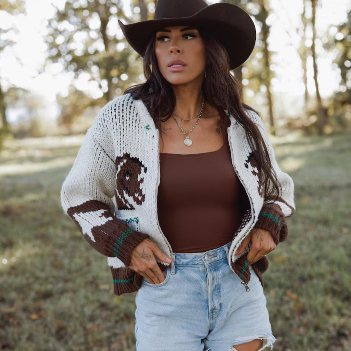 Woman wearing a patterned cardigan, brown top, and jeans outdoors.