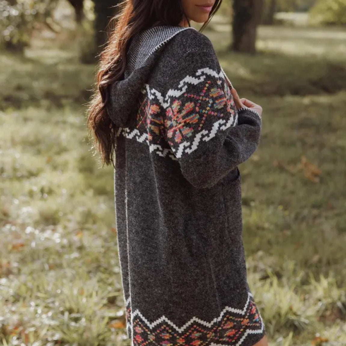 Person wearing a dark gray cardigan with patterned trim in an outdoor setting