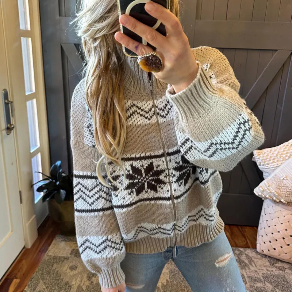 Person wearing a patterned sweater taking a mirror selfie indoors.