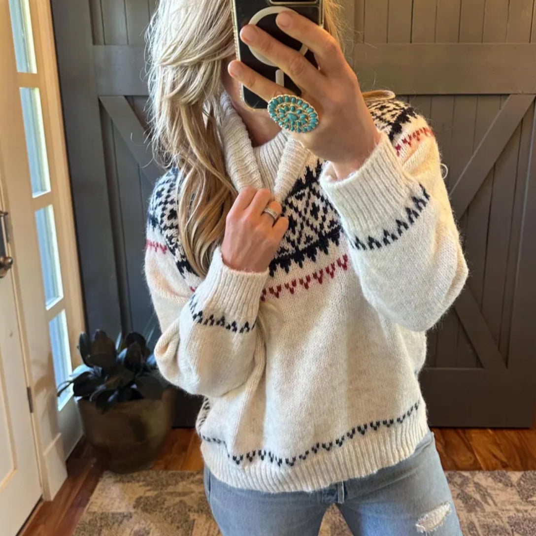 Person wearing a patterned sweater taking a mirror selfie indoors.
