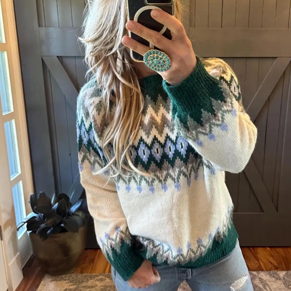 Person wearing a patterned sweater taking a mirror selfie indoors.