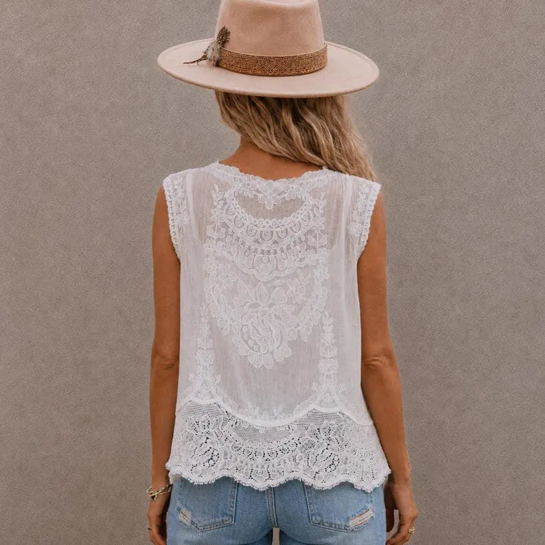A woman shown from the back wearing a sleeveless white lace top, a beige wide-brim hat, and light blue jeans against a textured gray wall.