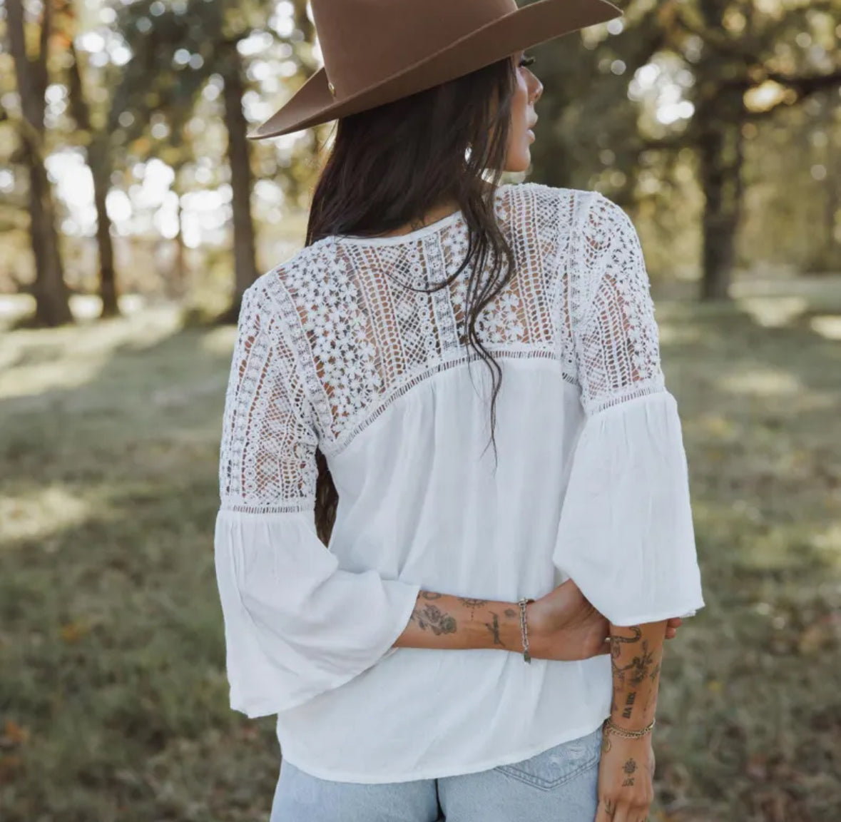 Woman wearing a white lace blouse and brown hat in a forest setting