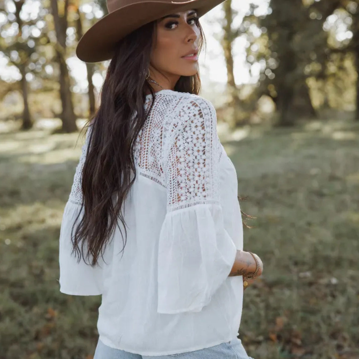 Woman wearing a white lace top and brown hat in a natural setting