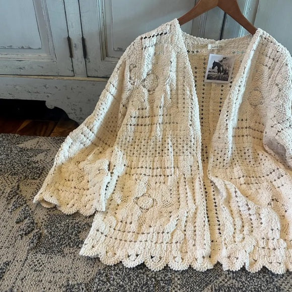 Beige crochet cardigan on a hanger with a wooden cabinet in the background