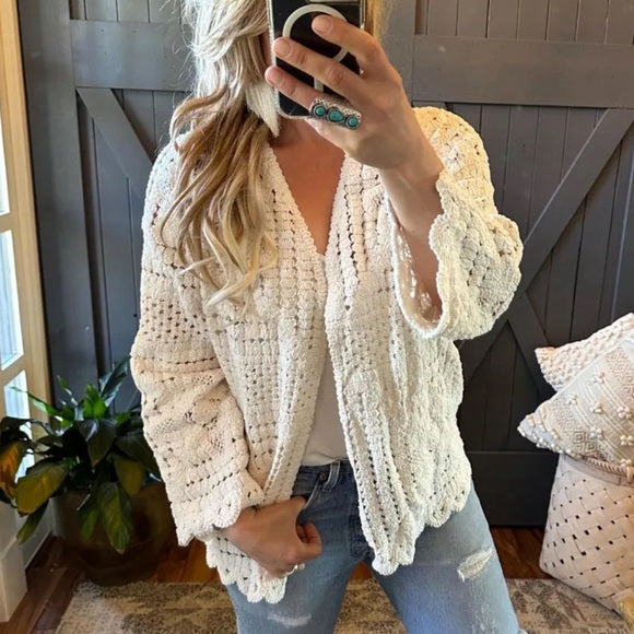 Person wearing a white crochet cardigan in a cozy indoor setting.