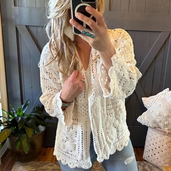Person wearing a beige crochet cardigan in a home setting.